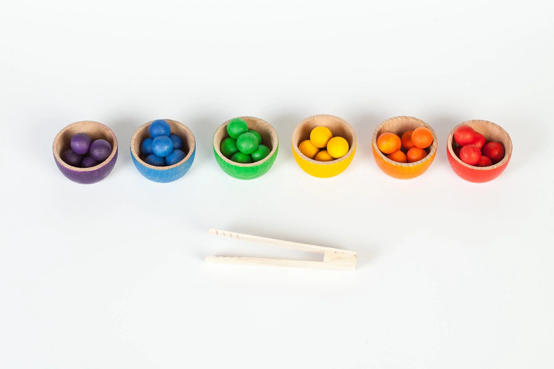 Set of colorful wooden bowls with small containers of multicolored objects on a white background