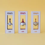 Three boxes of 'DROPS' spinning tops on a yellow background