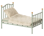 Small mint green metal bed with beige  and white bedding on a white background