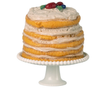 Layered cake with white frosting and fruit on top, placed on a white cake stand.