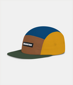 A color-blocked 5-panel cap by Headster with a blue top pane, yellow side panels, and a brown front panel. An olive green flat brim, shown on a light gray background.