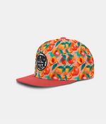 A snapback cap featuring a vibrant peach and orange fruit pattern on the crown with a solid coral-red flat brim. A circular black and white 'HEADSTER' logo patch is stitched on the front left panel.