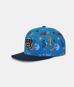 A blue snapback cap with a dark navy flat brim, featuring a playful cartoon pattern of colorful curvy crayons, stars, and doodles. A circular black and white patch on the side reads 'HEADSTER.