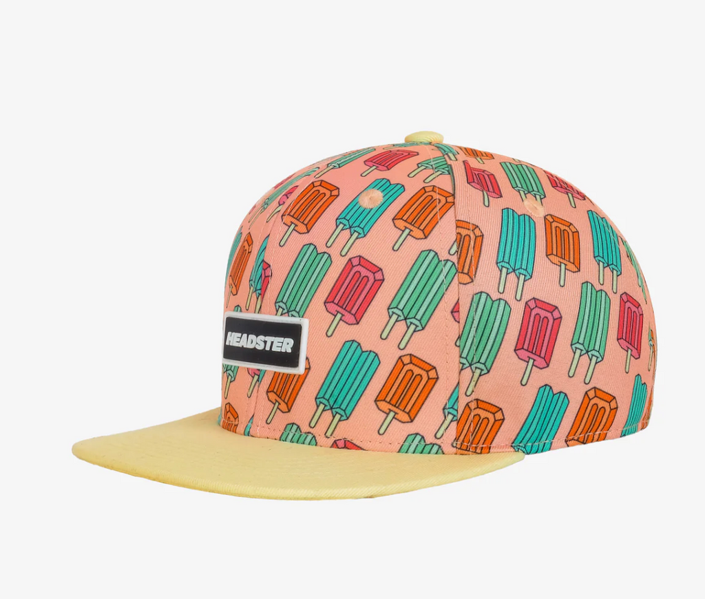 peach coloured snapback hat with high brim on a white background. Hat is covered with brightly coloured repeating popsicles. Brim is light yellow.