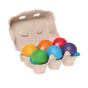 On a white background,  half an egg carton open to reveal six different coloured rainbow balls inside