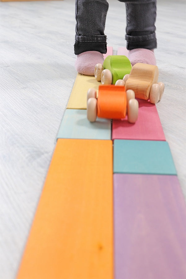 in interior photo of a child's feet and legs in the background standing of some wooden planks that are aligned to create a road that runs into the foreground. Wooden cars are on the planks.