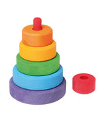 On a white background, a small wooden stacking tower with rings in rainbow colours. The top red piece is removed to reveal a red stick that the rings are stacked upon.