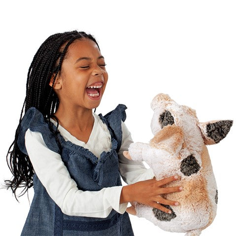 a girls with braids laughing and holding holding a a plush pink pig with grey spots on a white background