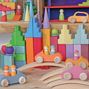 an assortment of grimms rainbow and pastel building blocks, cars and peg people in an interior space.