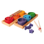 on a white background, two wooden trays with three different coloured bowls filled with matching wooden pieces in each. Two natural wooden tweezers one next to the tray, one on top of the bowls. Three purple wooden pieces next to one of the trays. 