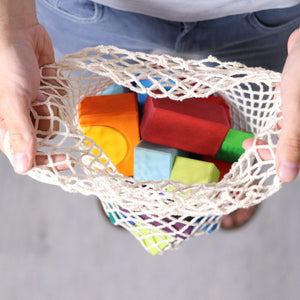A child holding the open net bag that is storing the blocks on a white background.