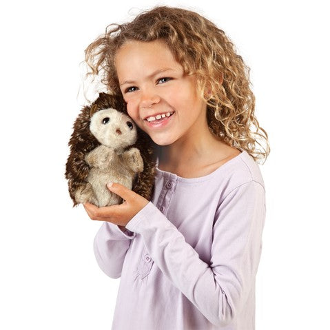 a girl with curly hair holding a plush hedgehog next to her face and smiling on a white background