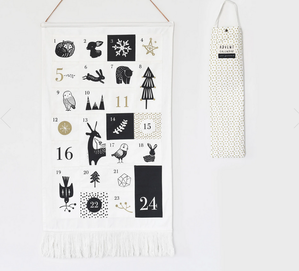 A black and white screenprinted canvas wall hanging with numbered pockets and graphic animal illustrations. There is fringe at the bottom and a sleeve style bag hanging next to the calendar on a white wall.hanging