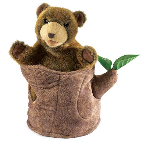 A brown, plush bear cub in a soft tree stump with two green leaves on a white background.