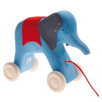 a wooden blue elephant on wheels with a red fabric over its back with leather ears held on by gold tacks. Painted eyes and a red string to be pulled from. On a white background