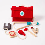 Five wooden and/or cotton doctor tools arranged in a white setting. Also shown is a red, cotton doctor's bag with a handle on top and a croos on the front