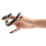 On a white background, a small plush snake wrapped around a person'd hand. A finger is inside a pocket at the front of the snake.